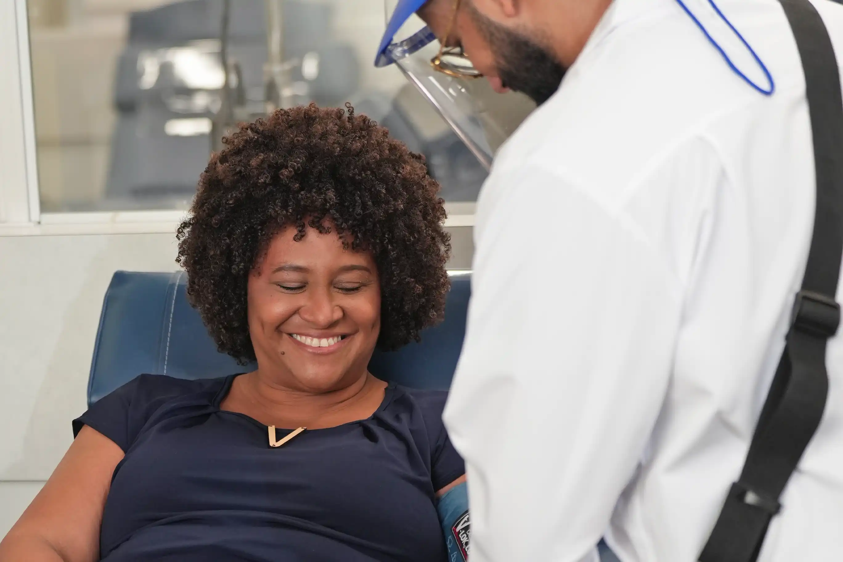 Una mujer donando plasma le sonría a su enfermero mientras la ayuda.